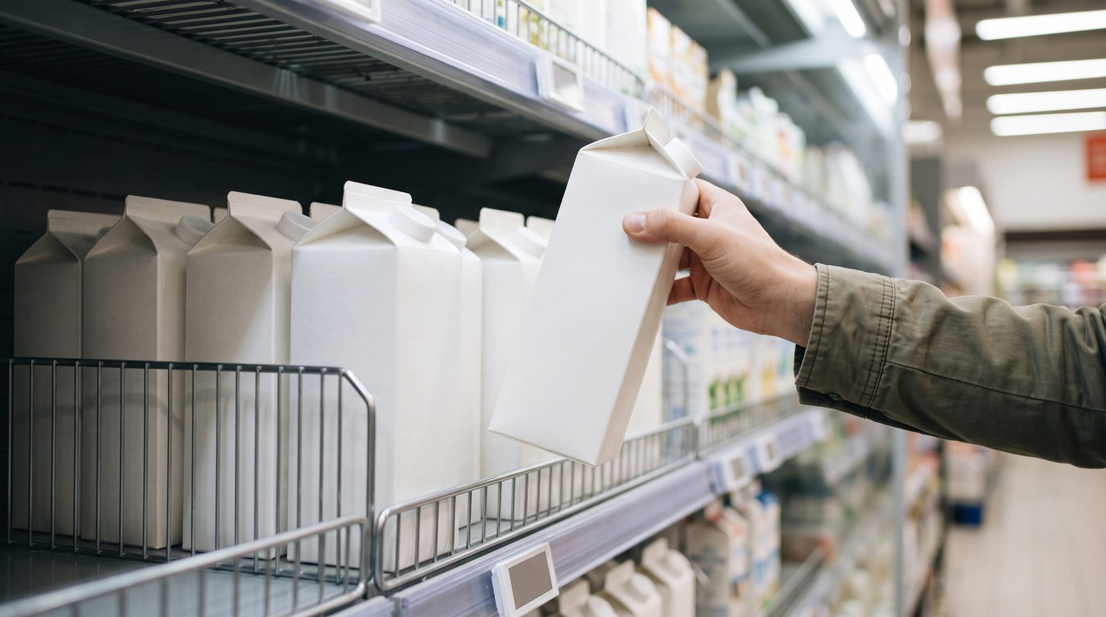 スーパーの乳製品売り場で牛乳パックを手に取る手元
